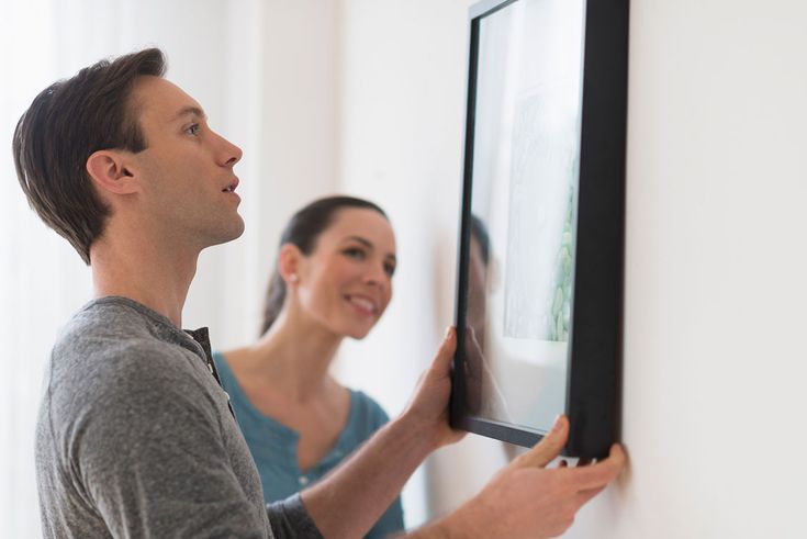 Man hanging a framed print on demand poster on a wall while a woman looks on.