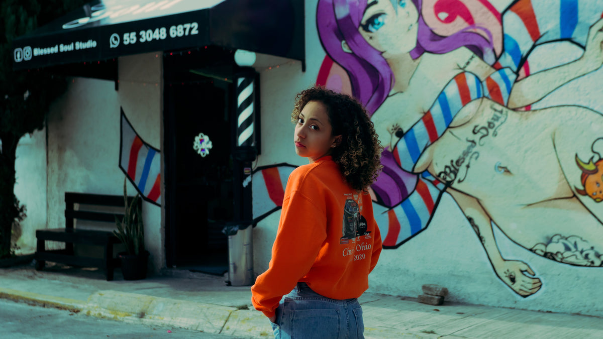 Woman wearing an orange print on demand sweatshirt in an urban setting with a graffiti background