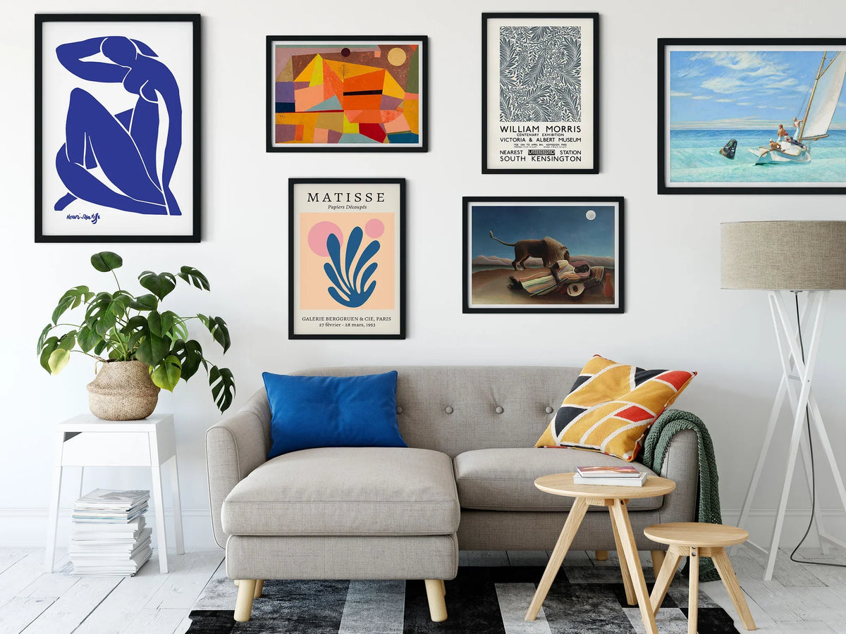 Modern living room with a grey sofa, colourful cushions, framed abstract artwork on the wall, a large potted plant, side table and floor lamp.